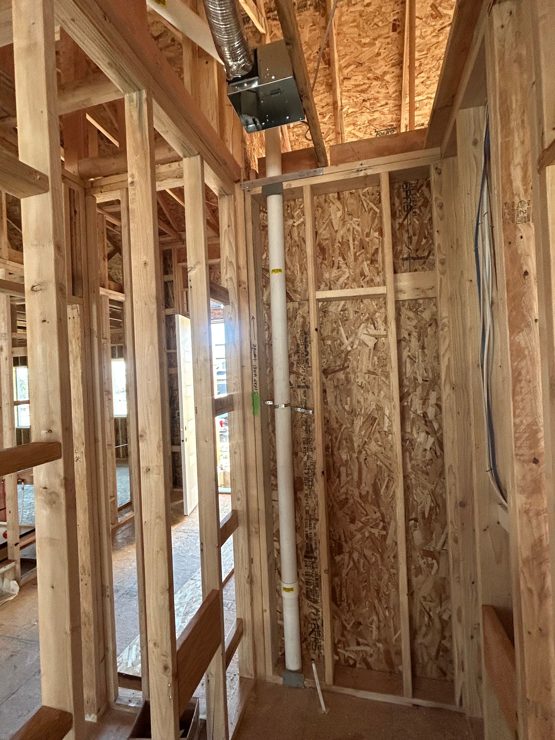 Interior of a wooden house frame under construction with exposed studs, beams, and plumbing pipes