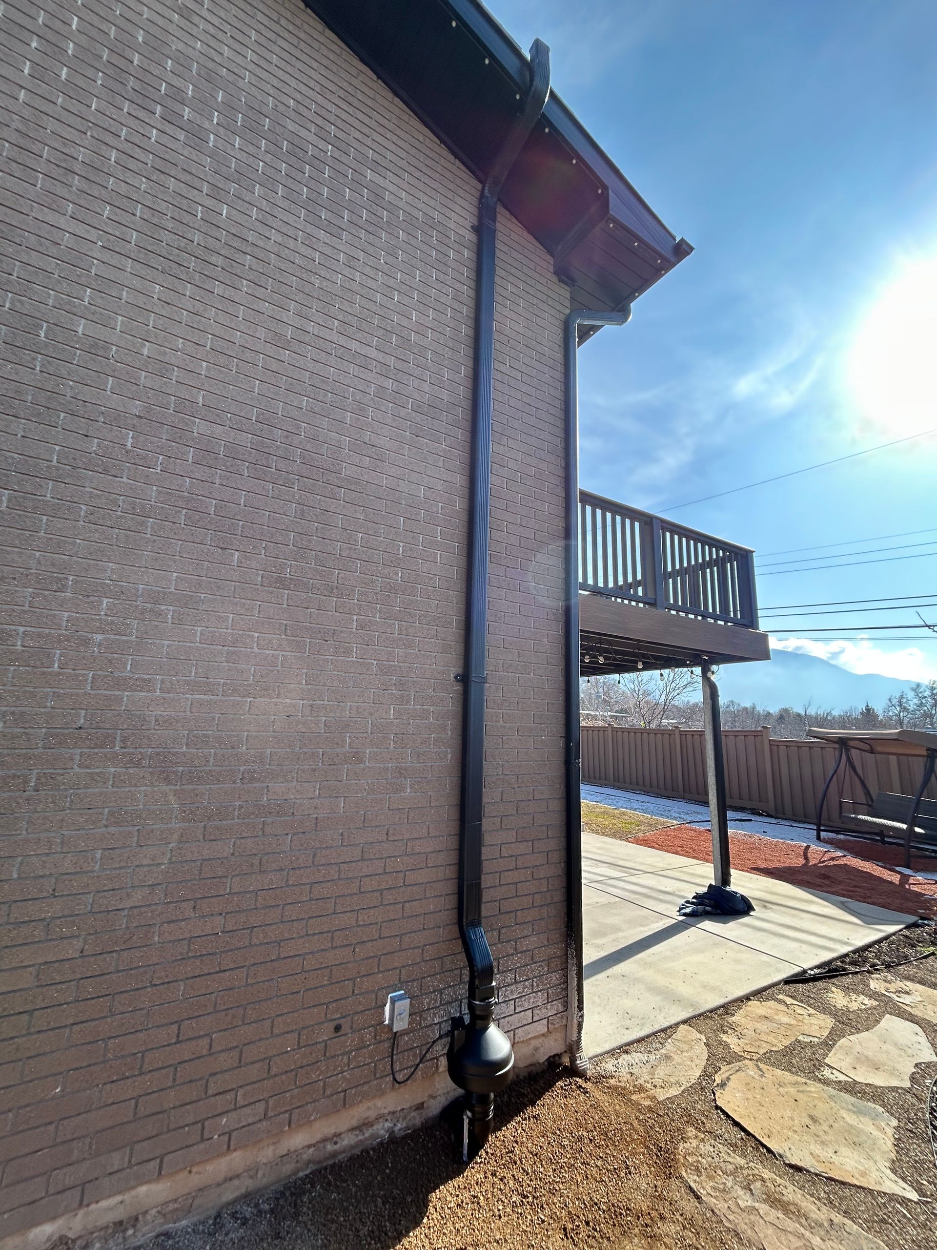 Brick house exterior with a side deck, concrete patio, and bright sun overhead