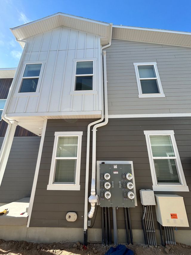 Two-story apartment building exterior with gray siding, white trim, utility meters, and bright blue sky