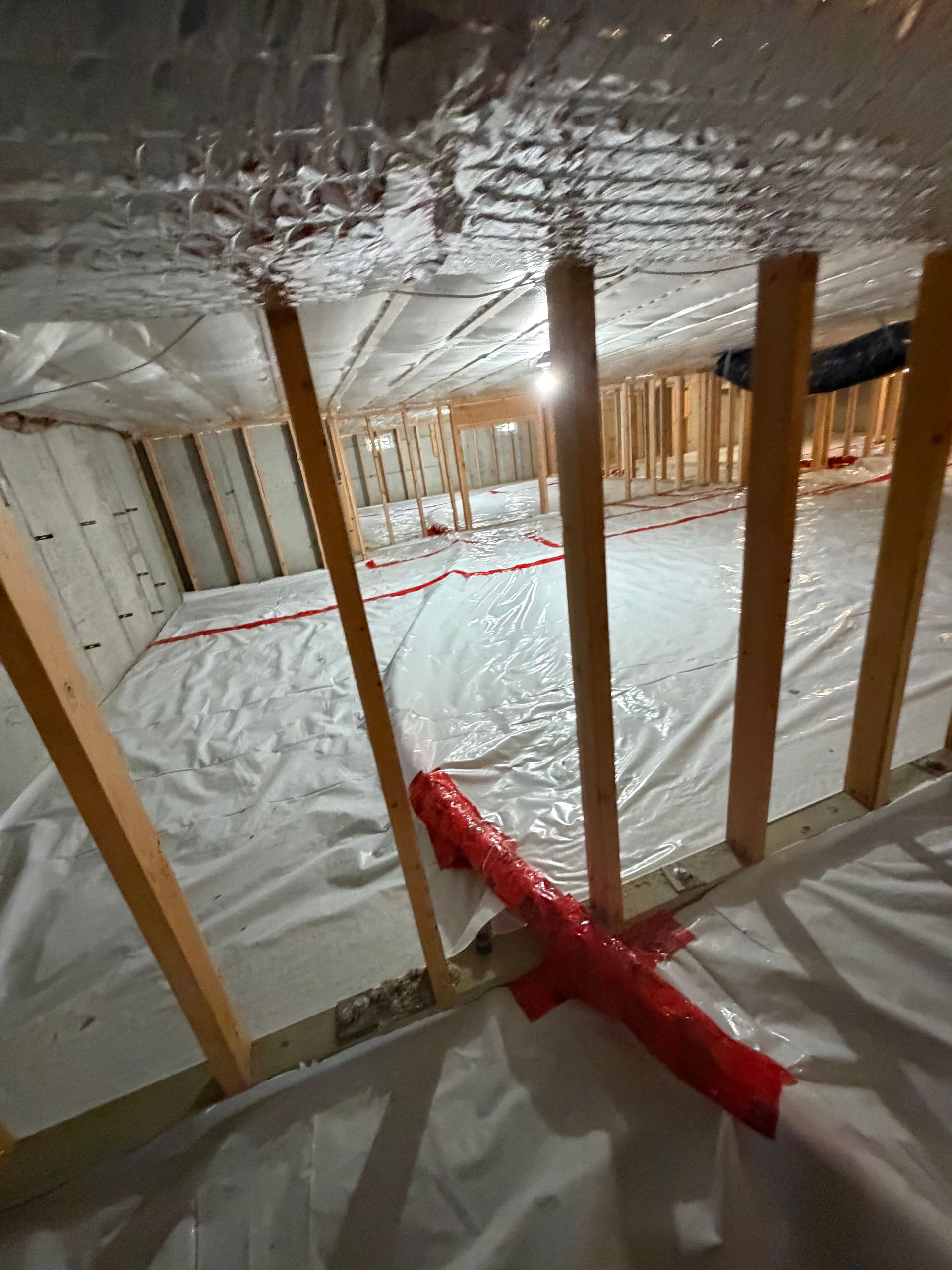 Unfinished attic with exposed wooden studs, white insulation, and red ductwork on the floor and ceiling.