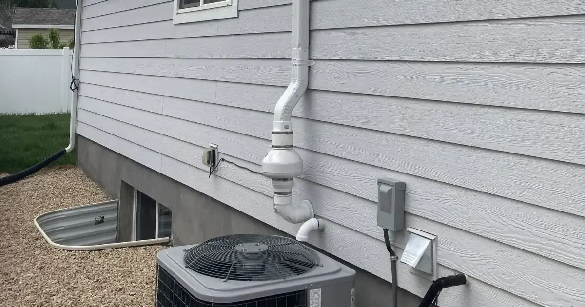 Side view of a house exterior with white siding, downspout, AC unit, and basement window well