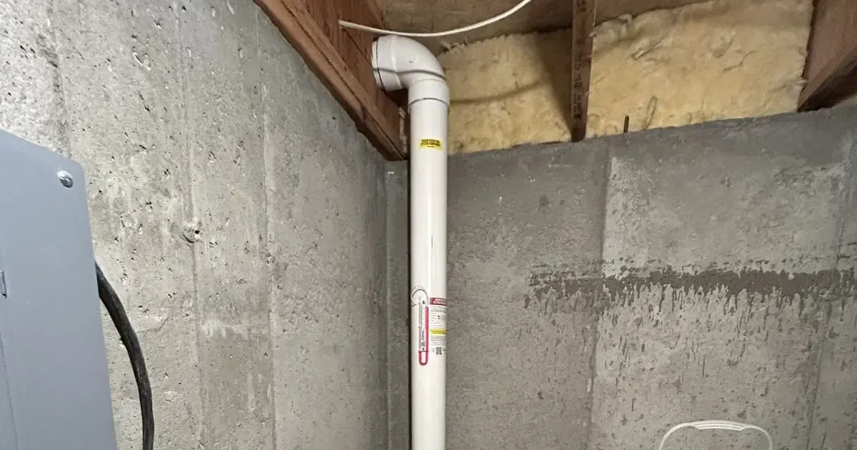 White PVC pipe with elbow joint in a concrete basement utility corner.