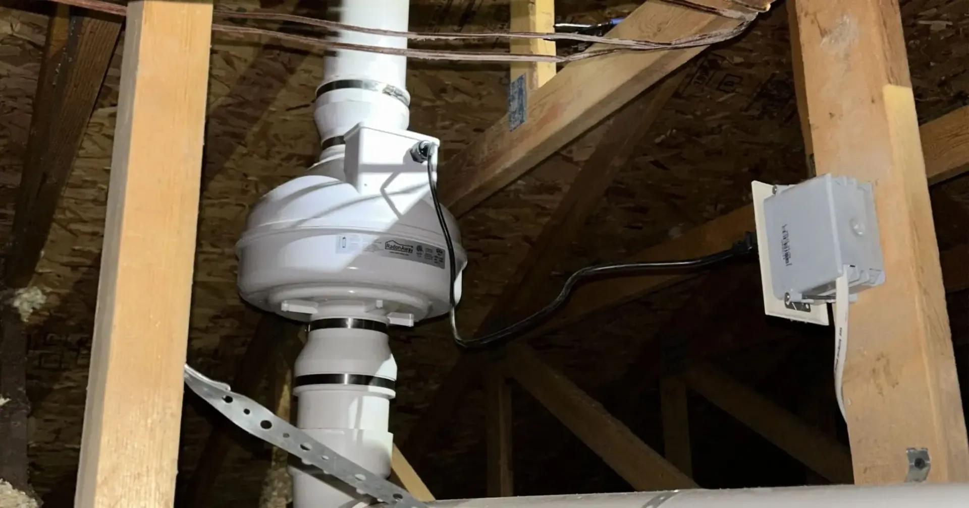 White ductwork and vent pipe in an unfinished attic with exposed wooden rafters.