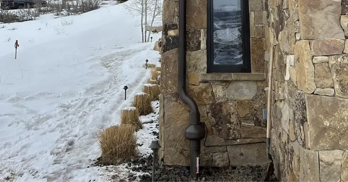 Snowy path beside a stone house wall with a window and downspout