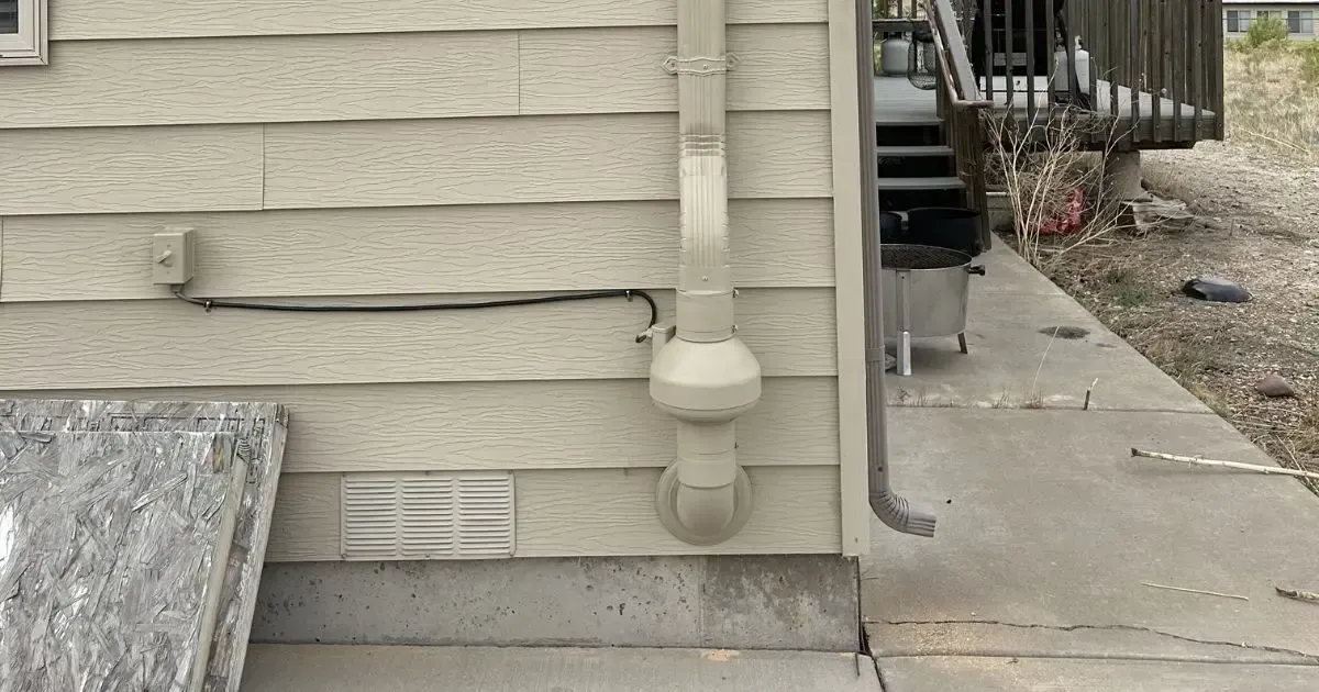 Exterior house wall with beige siding, downspout, vent, and concrete walkway along the side yard