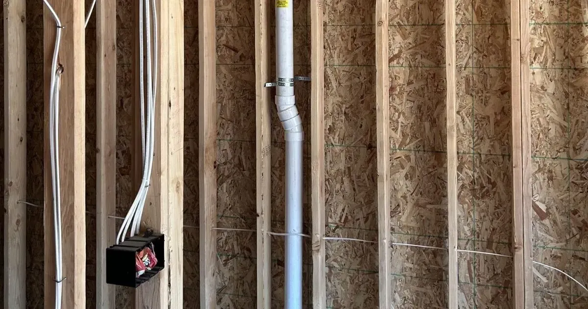 Exposed wooden wall studs with electrical wiring and a black junction box in a construction site interior