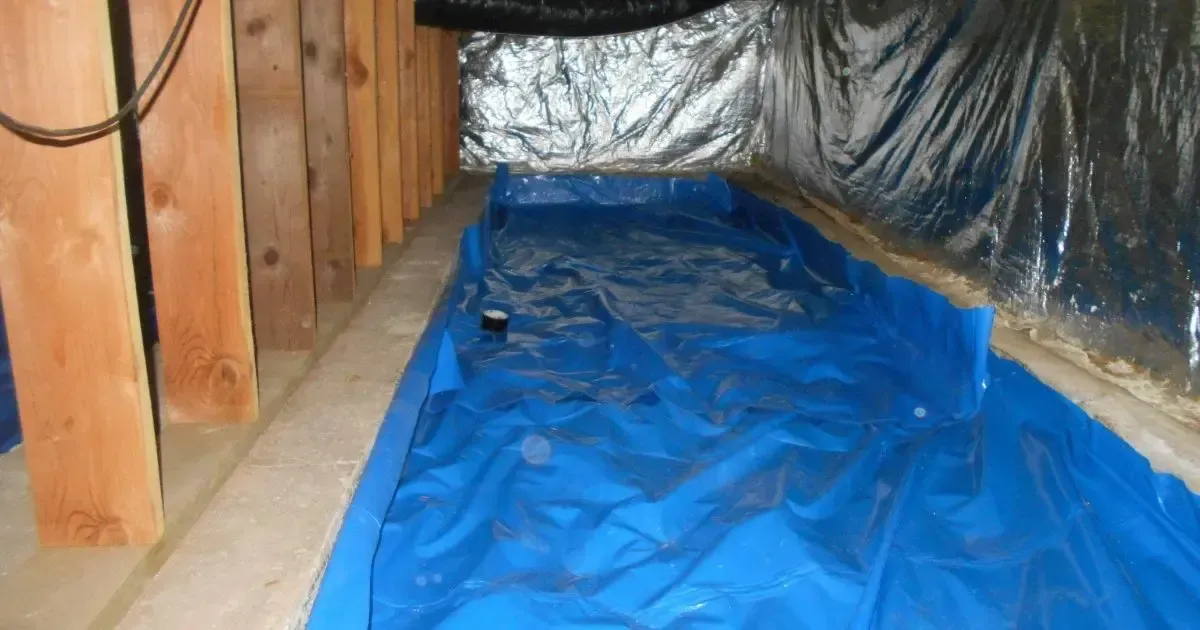 Blue tarp lining a crawlspace floor beside wooden posts and black insulation