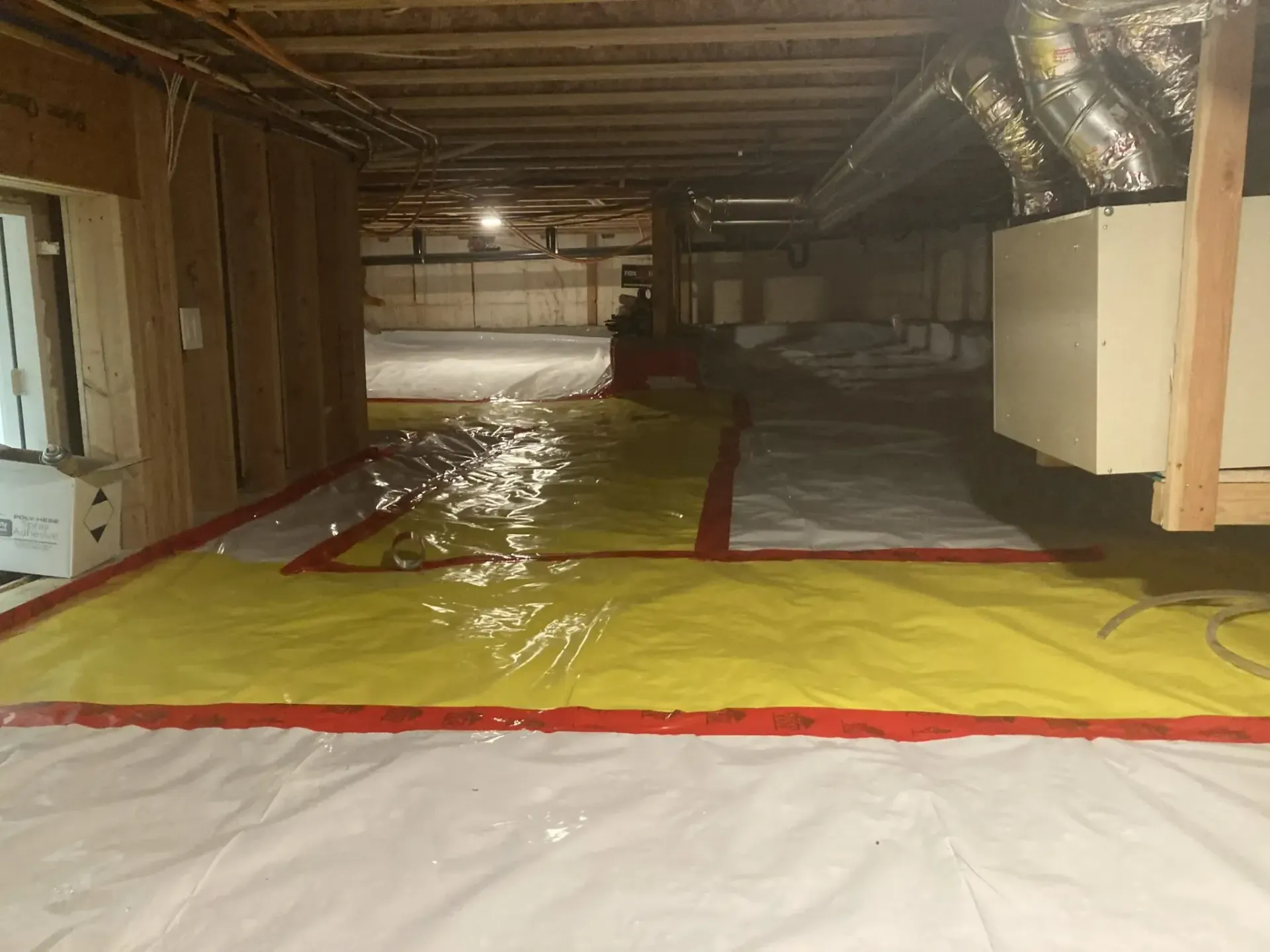 Basement crawlspace with yellow and white floor vapor barrier under exposed beams and ducting