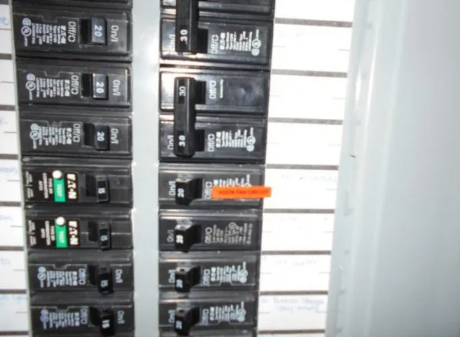Electrical breaker panel with rows of black circuit breakers, one switched in orange.