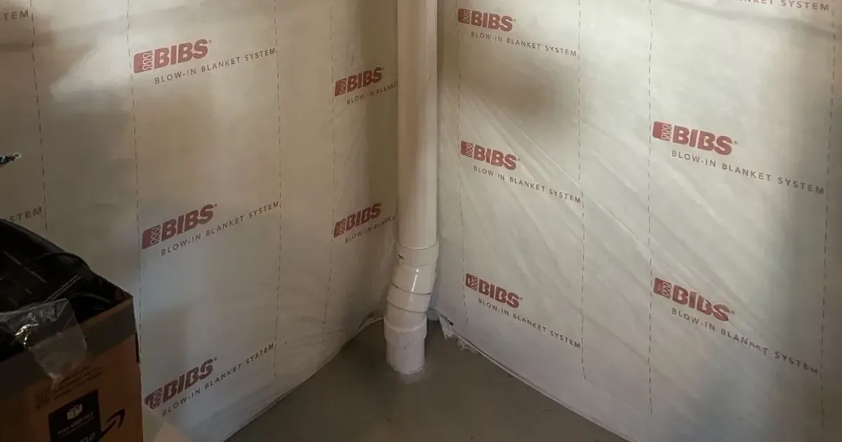 Interior corner wrapped in white insulation panels with red logos, beside a small stack of pipes and a dark box.
