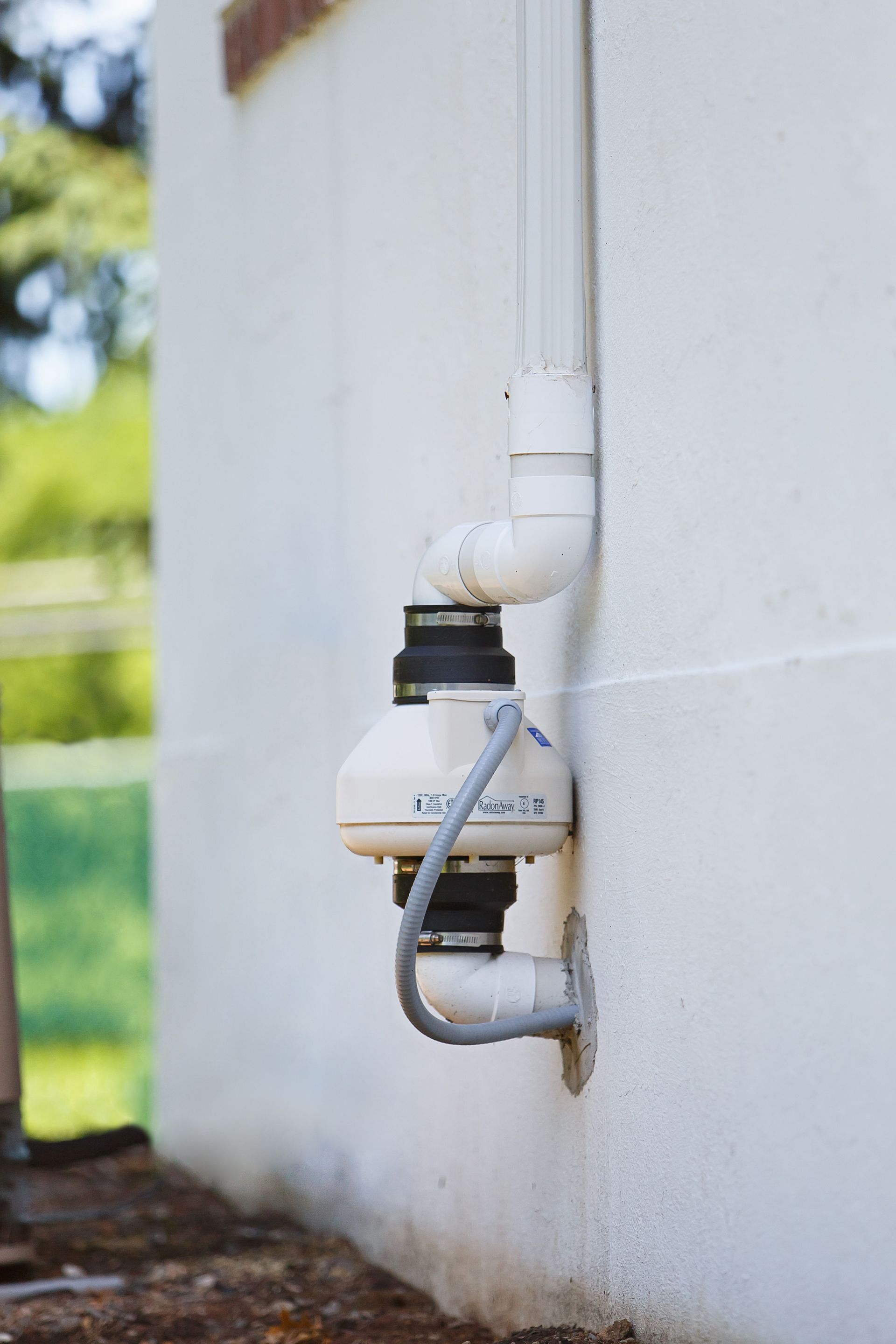 White wall-mounted utility meters and pipes outdoors beside a building.