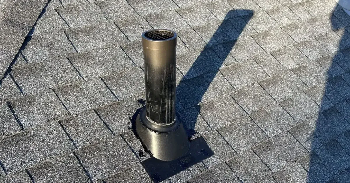 Metal roof vent pipe on gray shingles in sunlight