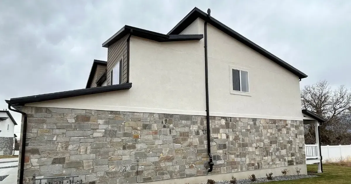 Stone-and-plaster house exterior with a black roof and white upper walls on a cloudy day