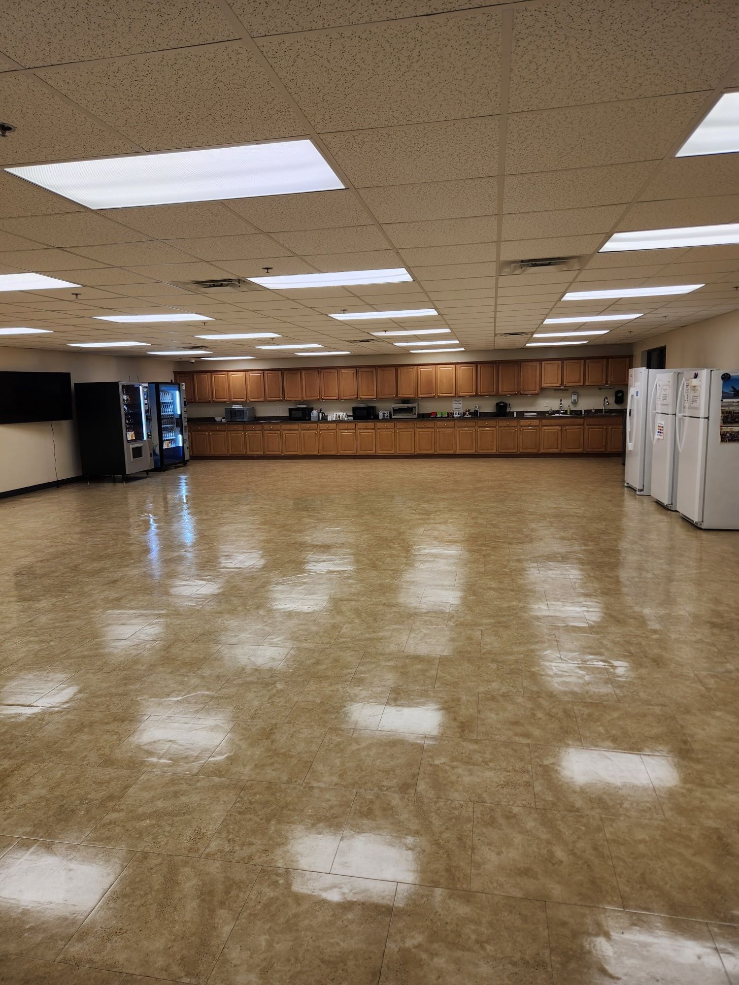 Empty room with linoleum floor, overhead lights, and a long counter with cabinets and appliances.