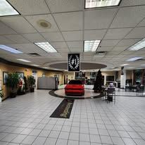 A red car is parked in the middle of a large room in a car dealership.