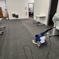 A blue vacuum cleaner is sitting on a carpeted floor in a room.