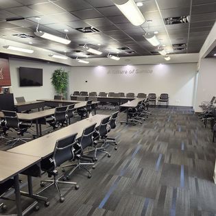 A large conference room with tables and chairs and a tv on the wall.