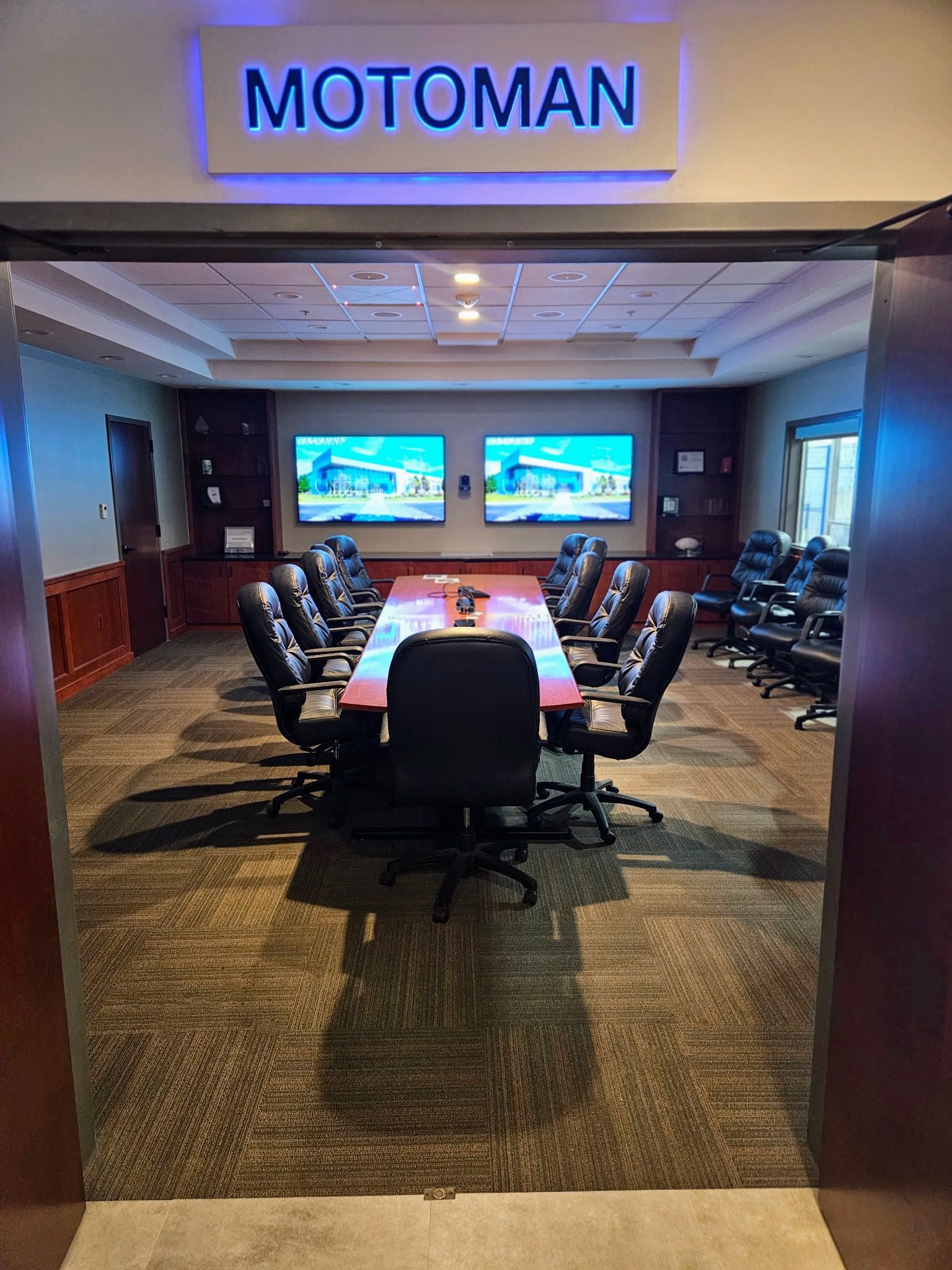 A large conference room with a long table and chairs and a sign that says motoman.