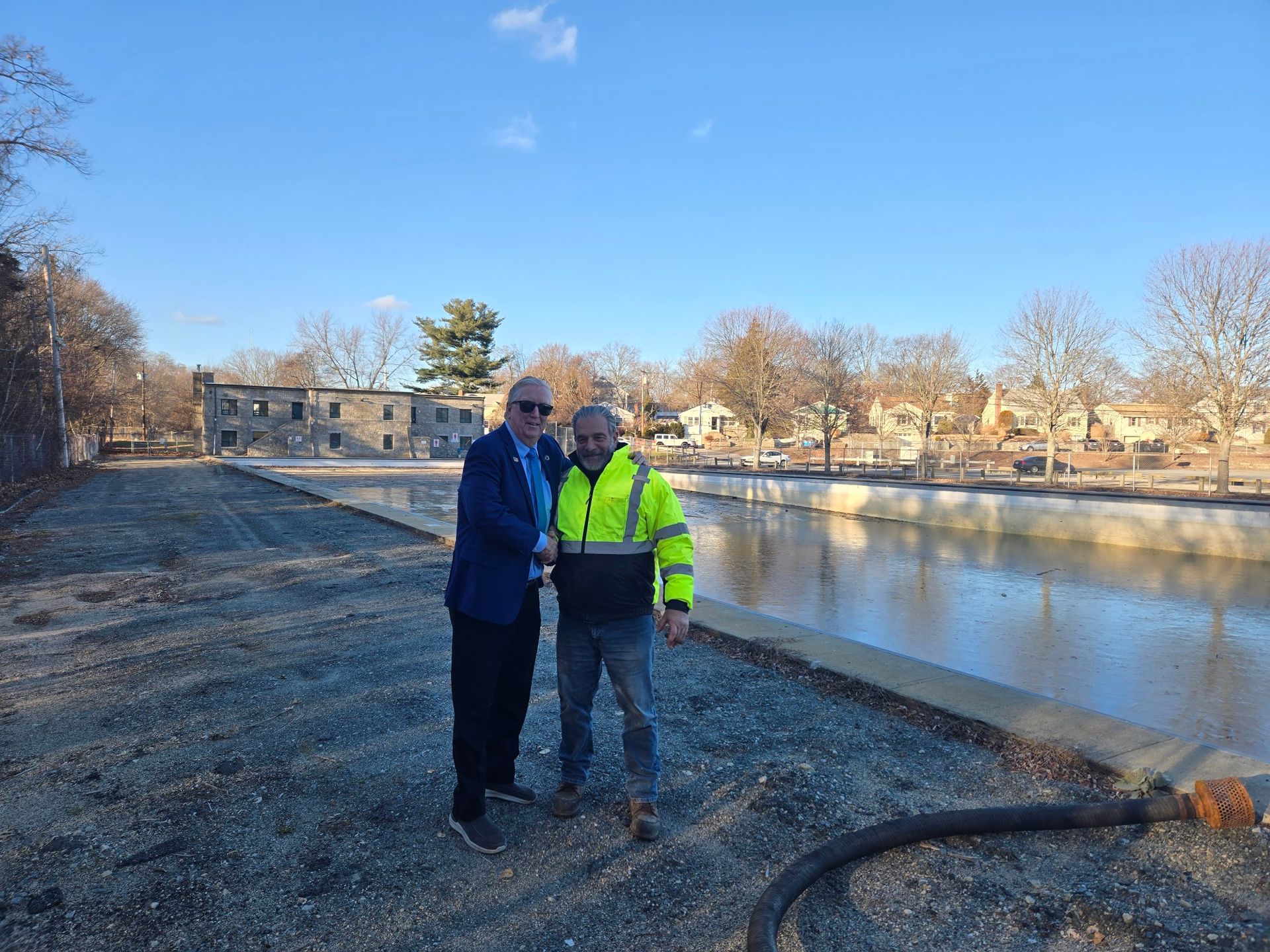 Two people standing on a gravel path beside a river on a clear day