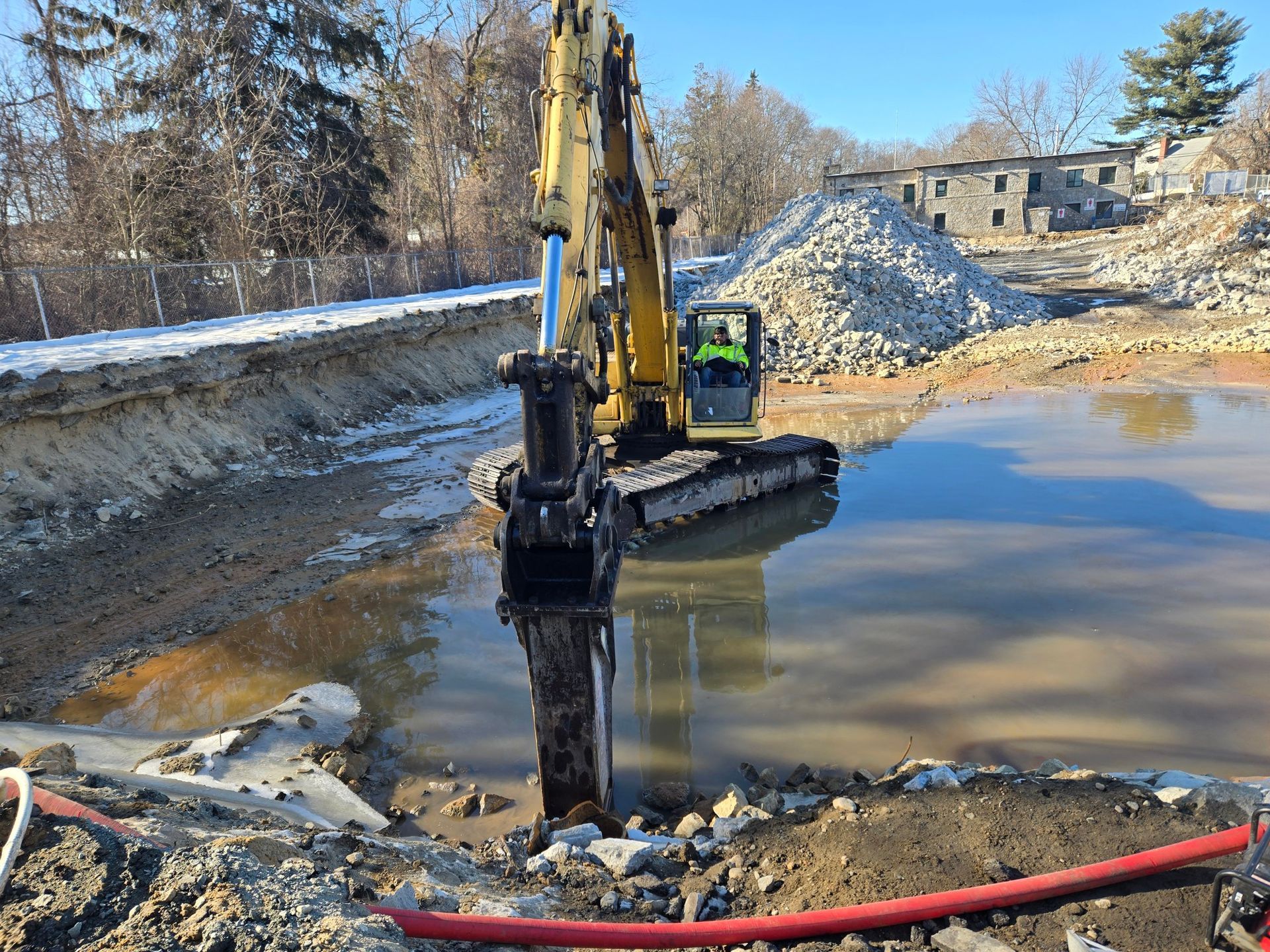 Yellow excavator working beside a muddy water pit at a snowy construction site