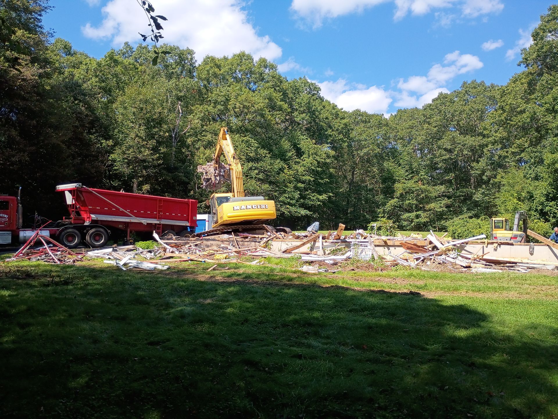 Construction site with excavator and red dump truck clearing debris in a wooded area