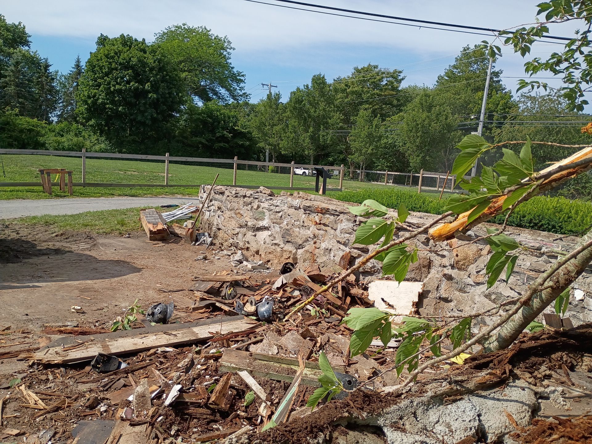 Collapsed concrete wall with rubble and fallen branches beside a road in a park-like area