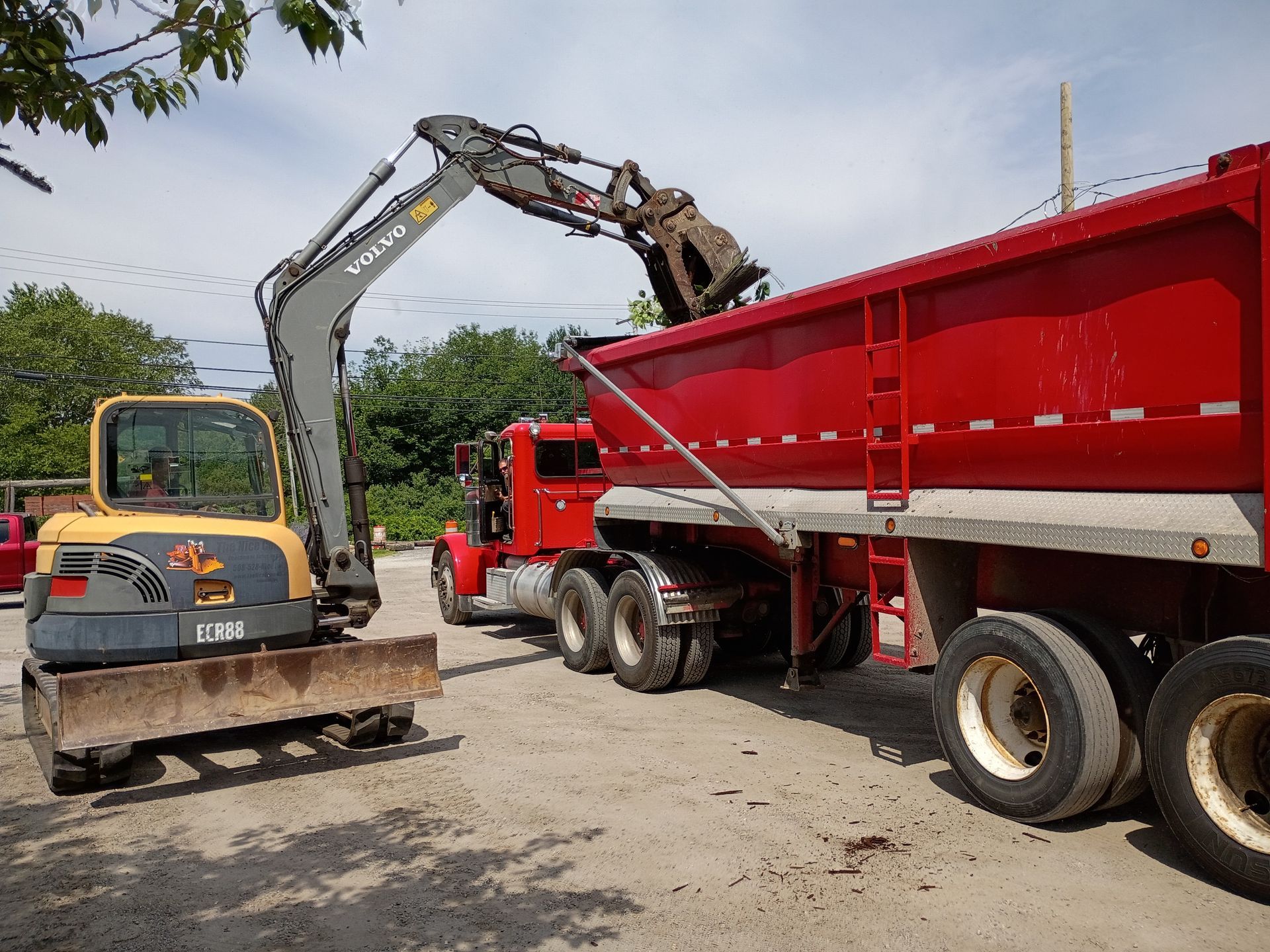 Excavator loading dirt into a red dump truck at a construction site