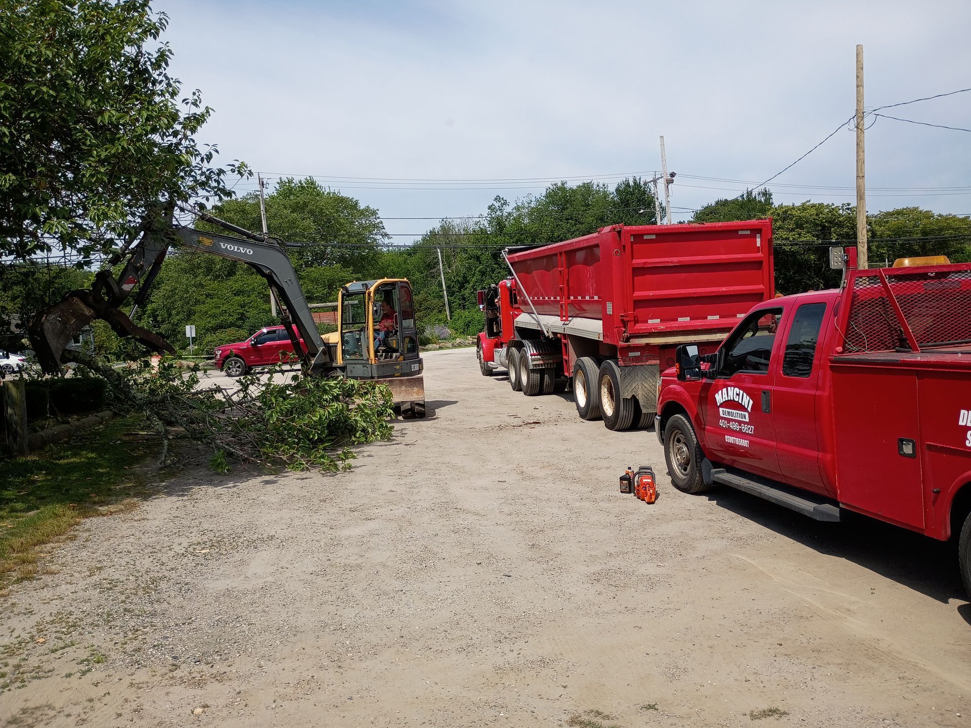 Red dump trucks and a red pickup parked on a dirt road at a worksite, with a small excavator nearby.