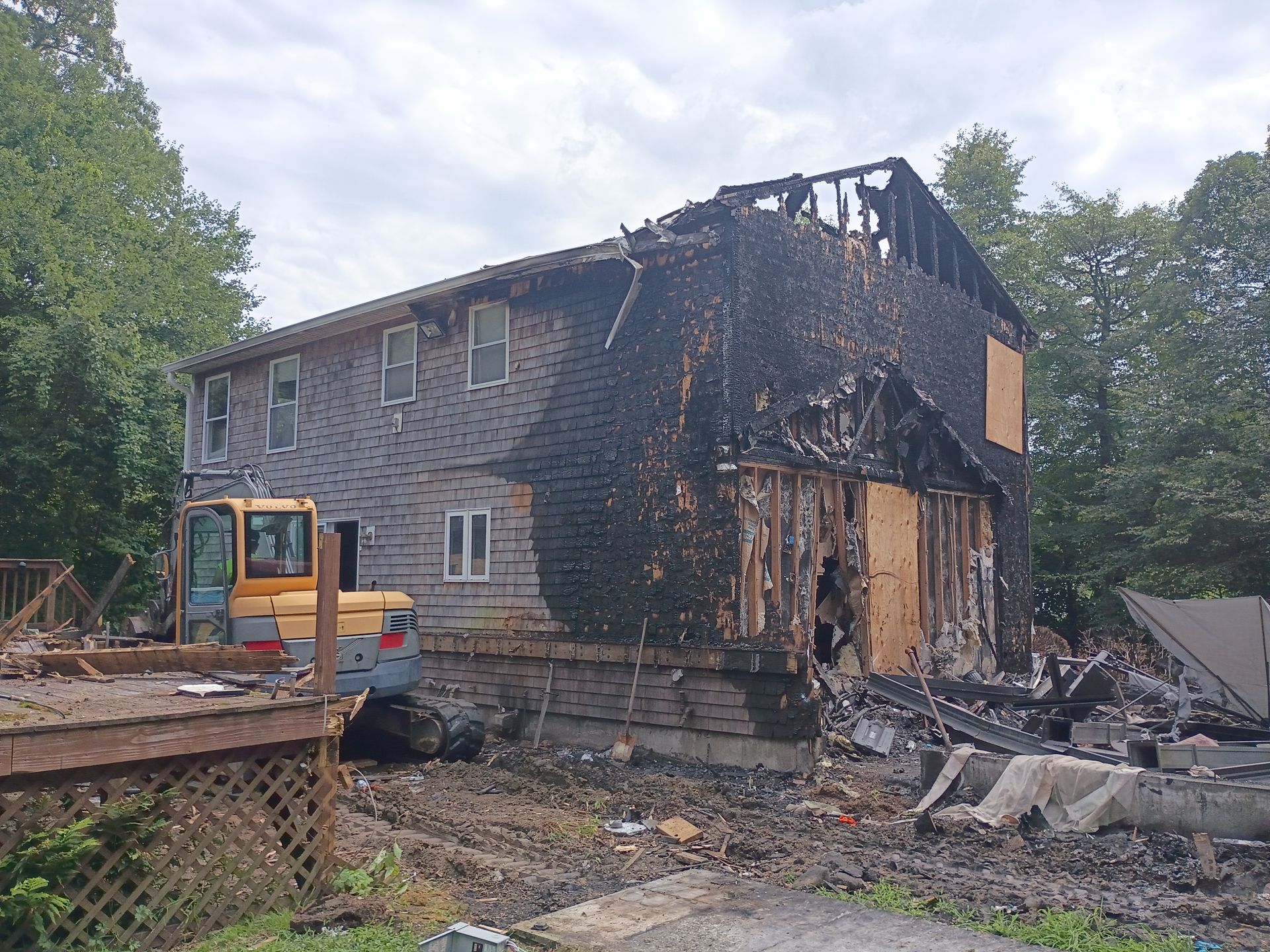 Charred house remains after fire, with a small excavator and debris in the yard