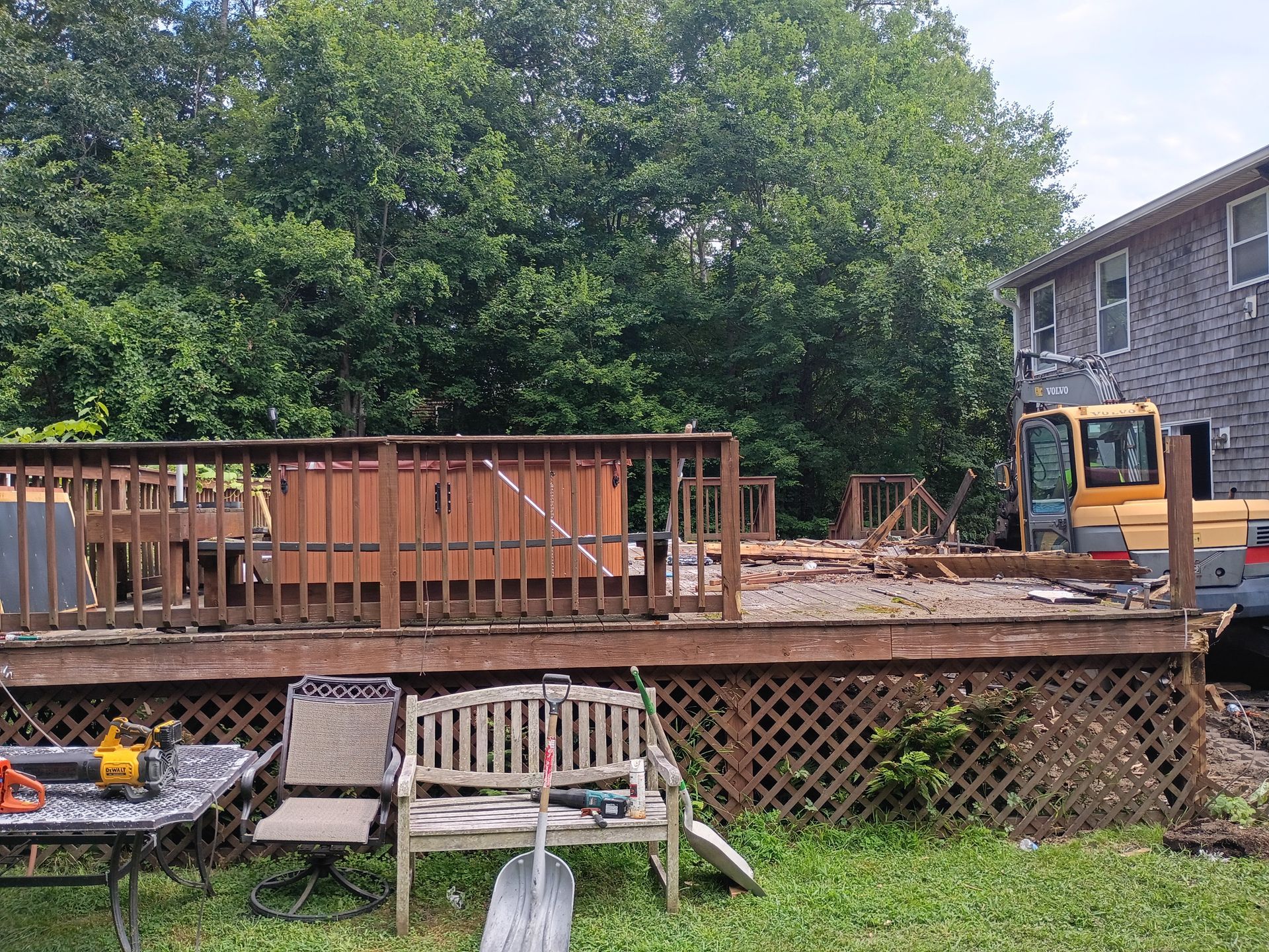 Backyard deck under construction with wooden railing, bench, and orange excavator beside a house