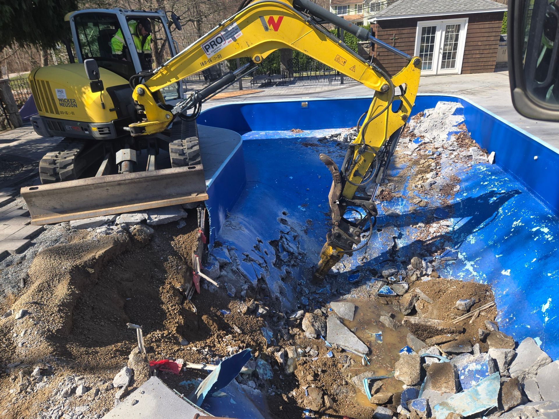 Mini excavator dumping muddy debris into a large blue container on a construction site