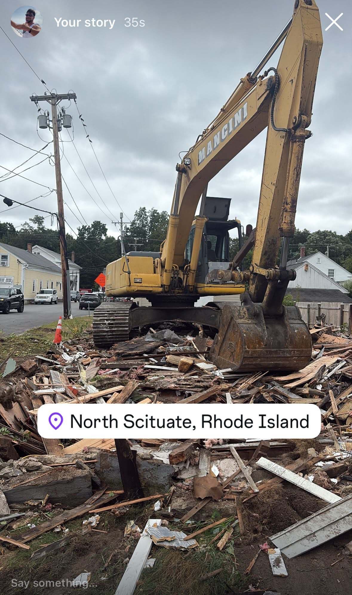 Yellow excavator amid roadwork debris on a street in North Scituate, Rhode Island.