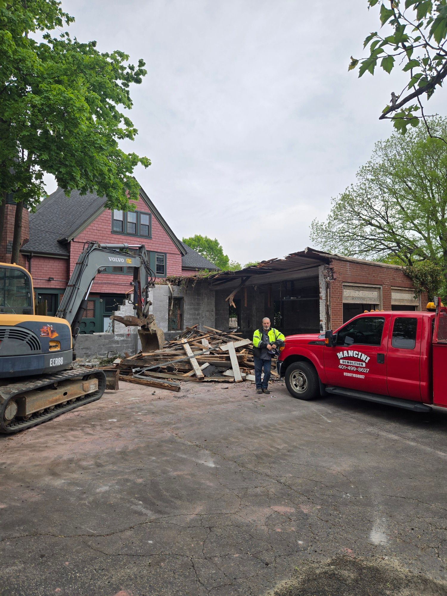 Damaged building with rubble, construction workers, and red and black work trucks at a demolition site