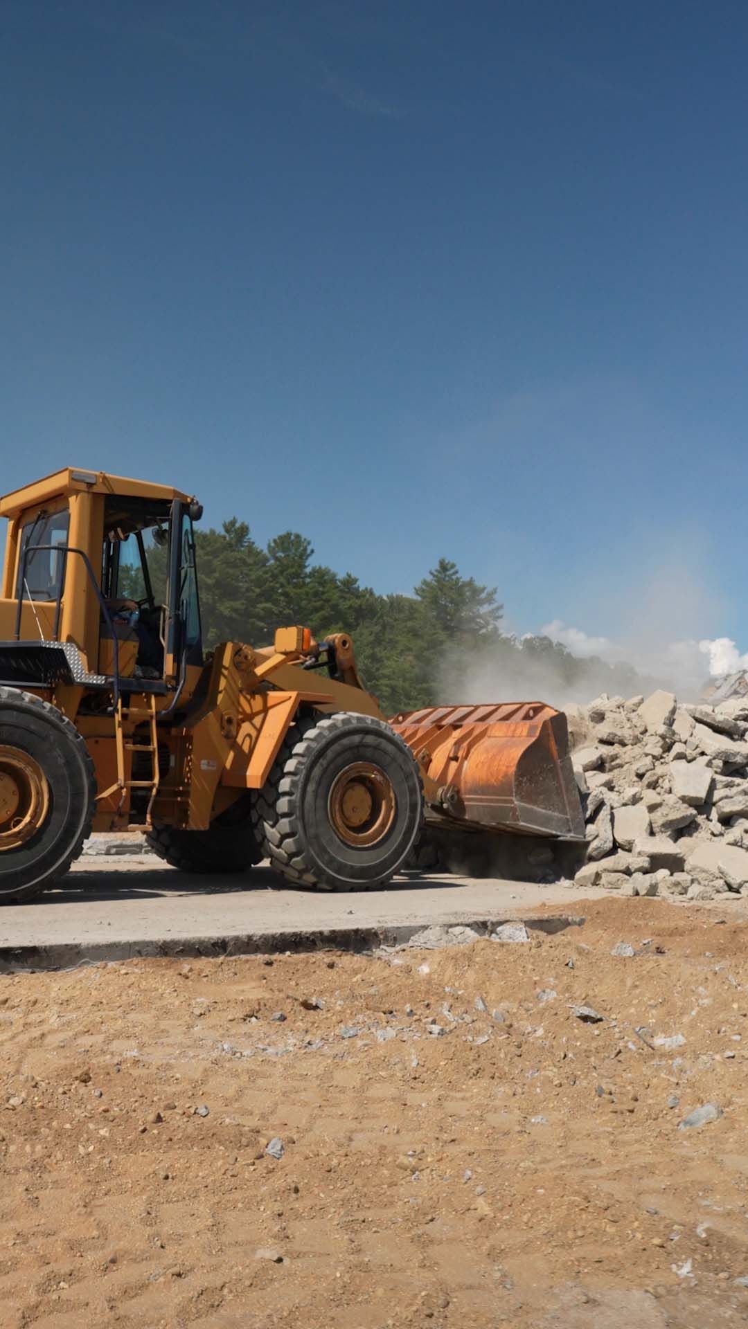 Orange front loader moving rubble at a dusty construction site