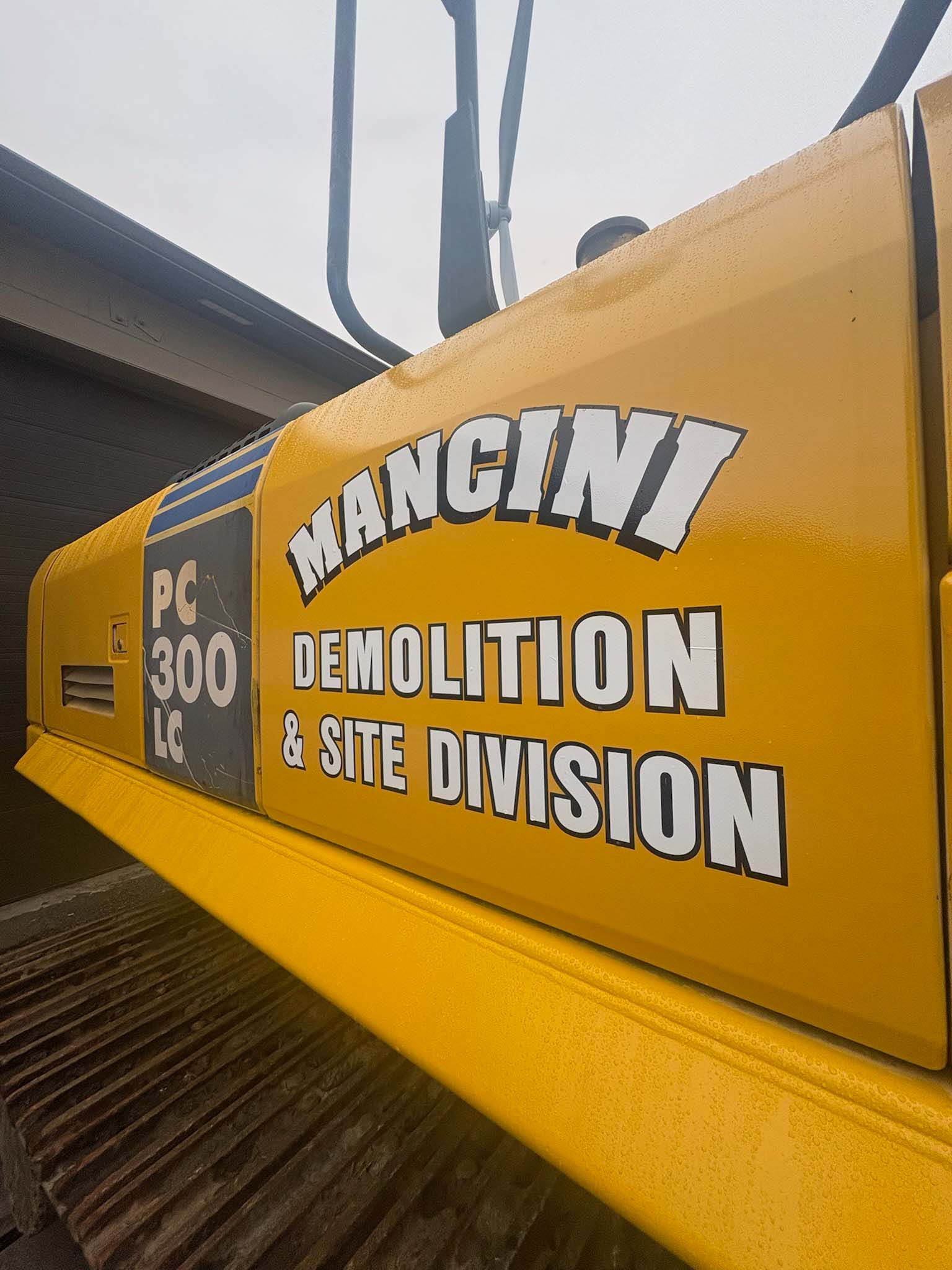 Yellow excavator with “MANGLOVE DEMOLITION & SITE DIVISION” logo on the arm