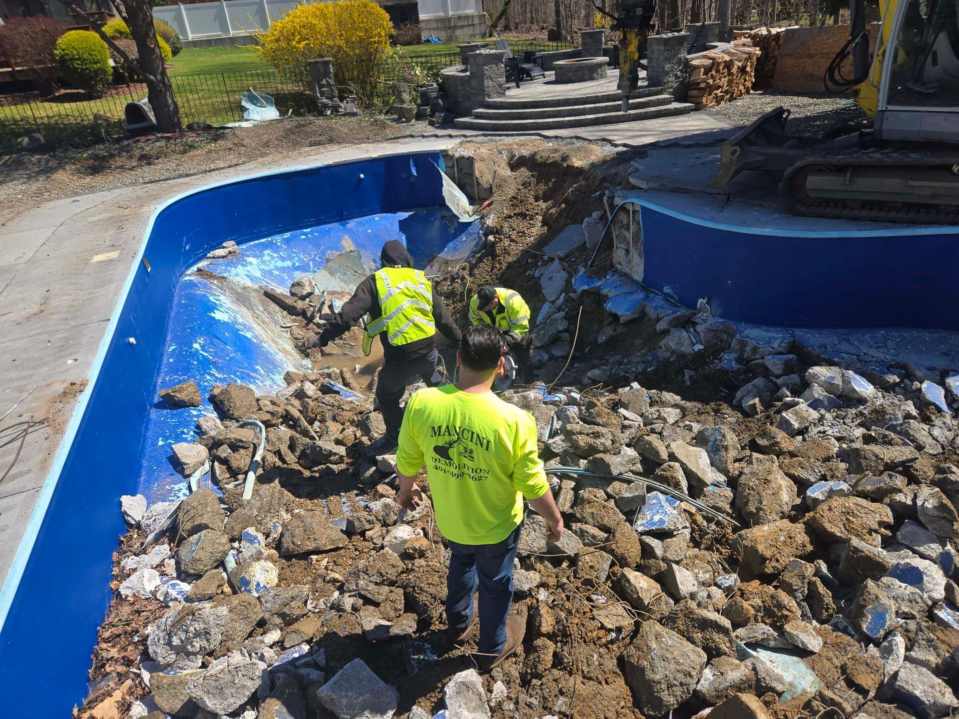 Workers clearing rubble from a damaged blue pool in a yard