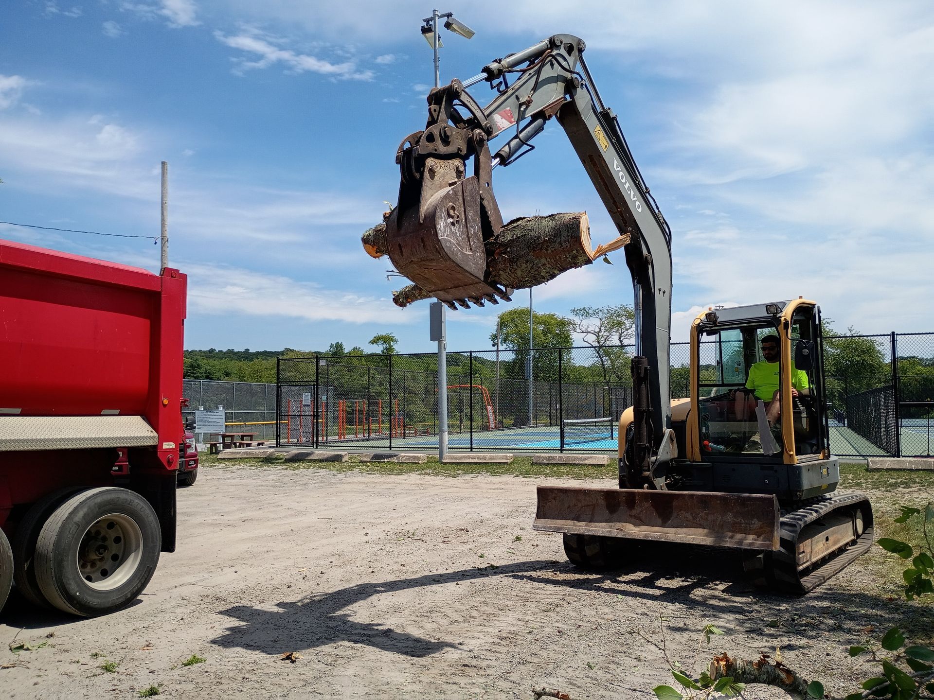 Excavator lifts a large bucket beside a red dump truck on a construction site.