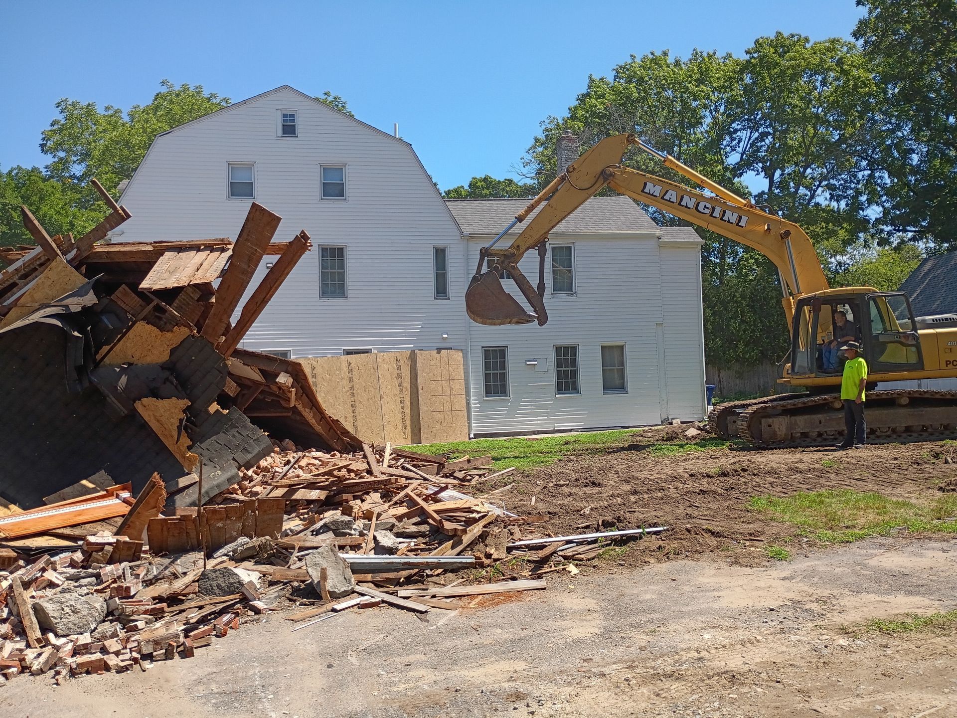 Demolition of a white house with an excavator tearing down the left side amid rubble