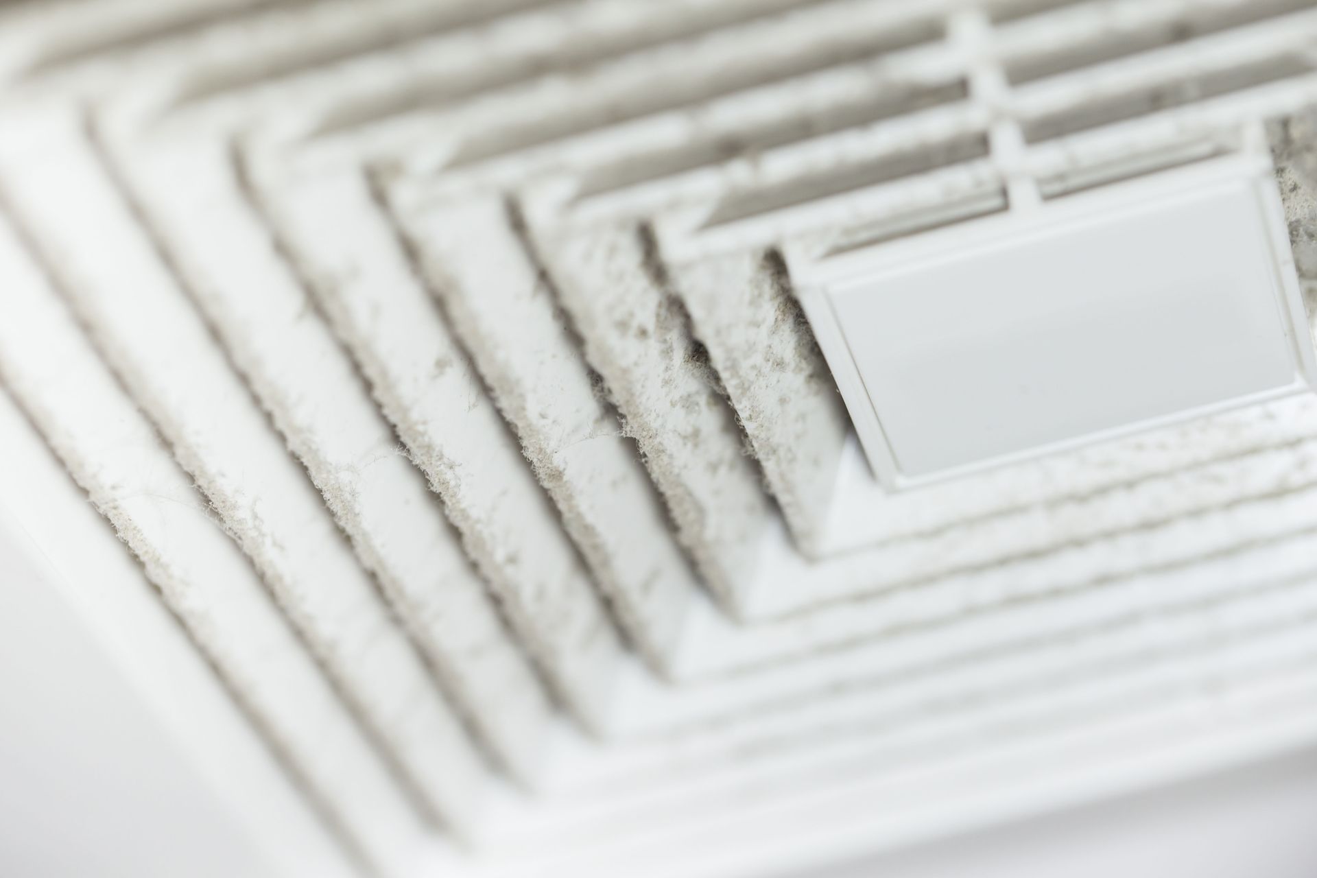 Close-up of a white, dusty air vent cover in a ceiling.