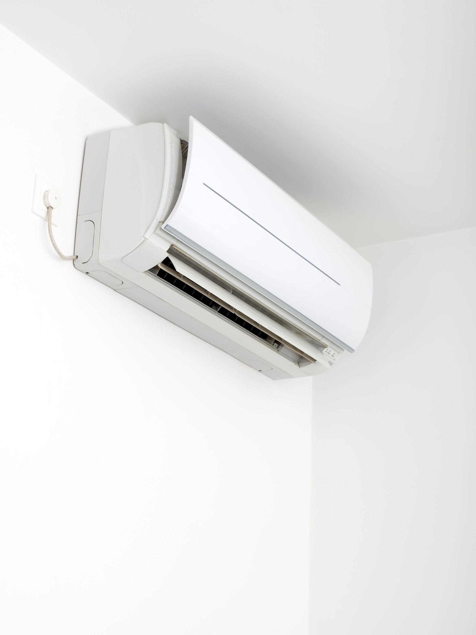 White wall-mounted air conditioning unit in corner of white room.