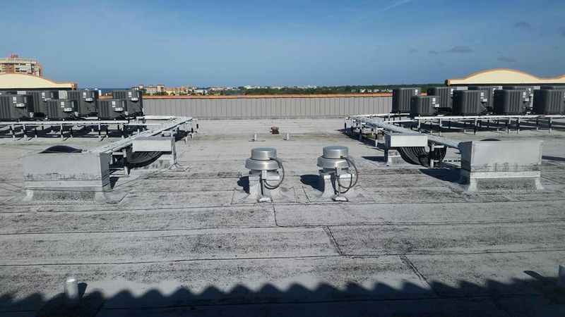Rooftop with HVAC units, vents, and a metal barrier. Gray and white surfaces under a blue sky.