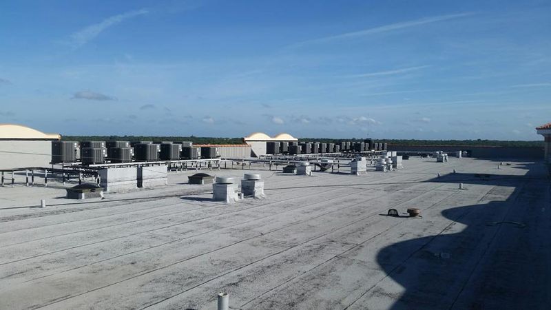 Flat commercial roof with HVAC units and vents against a blue sky.