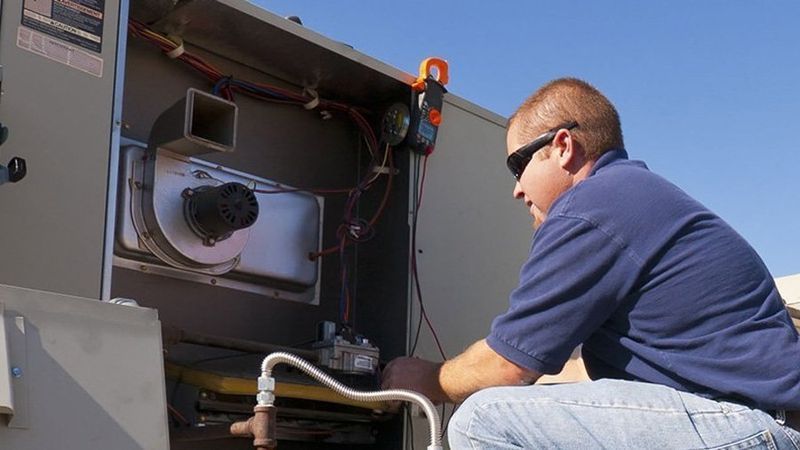 HVAC technician working on an air conditioning unit outside, using a multimeter.