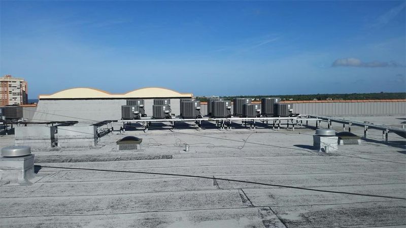 Rooftop view of commercial building, HVAC units, blue sky, and vents.
