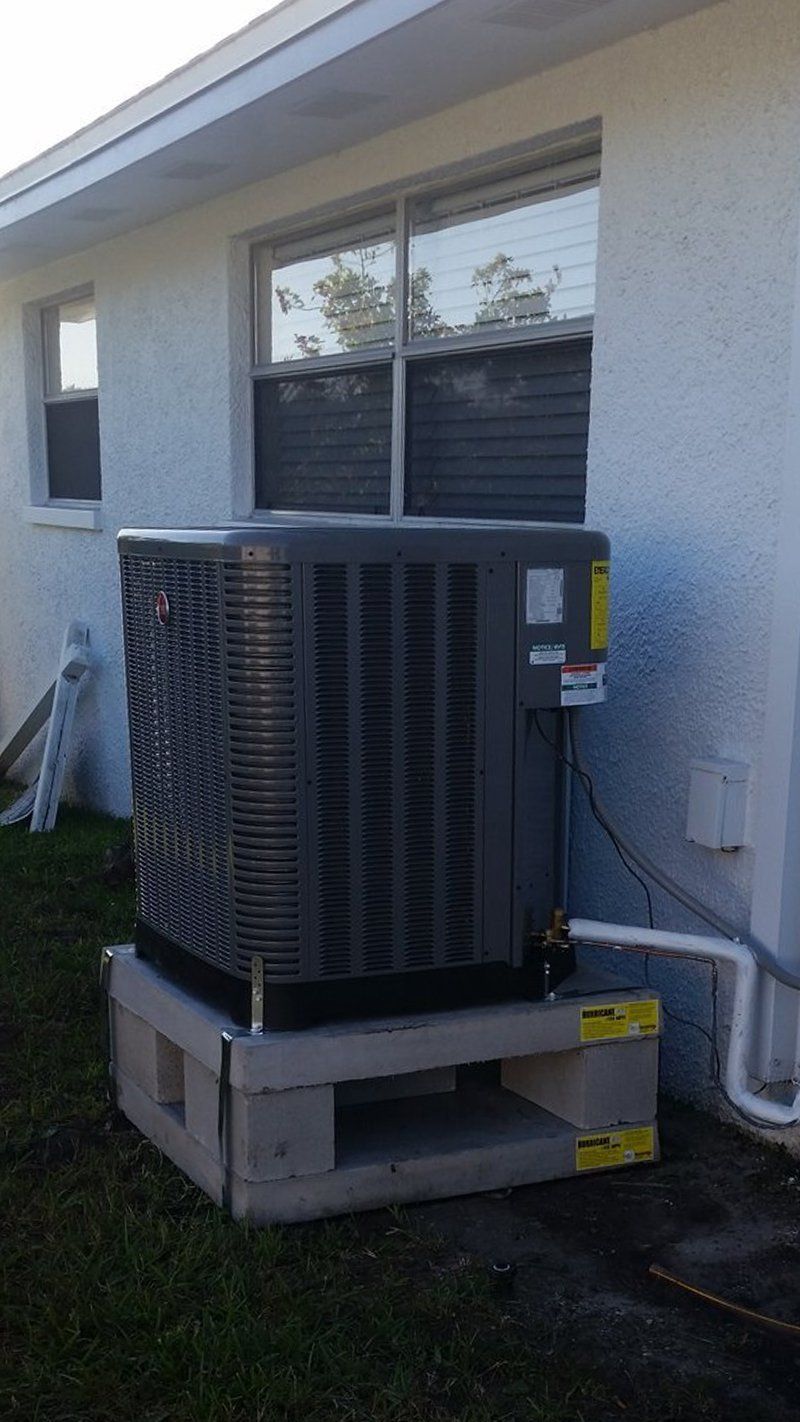 Air conditioning unit on concrete block base next to a white house.