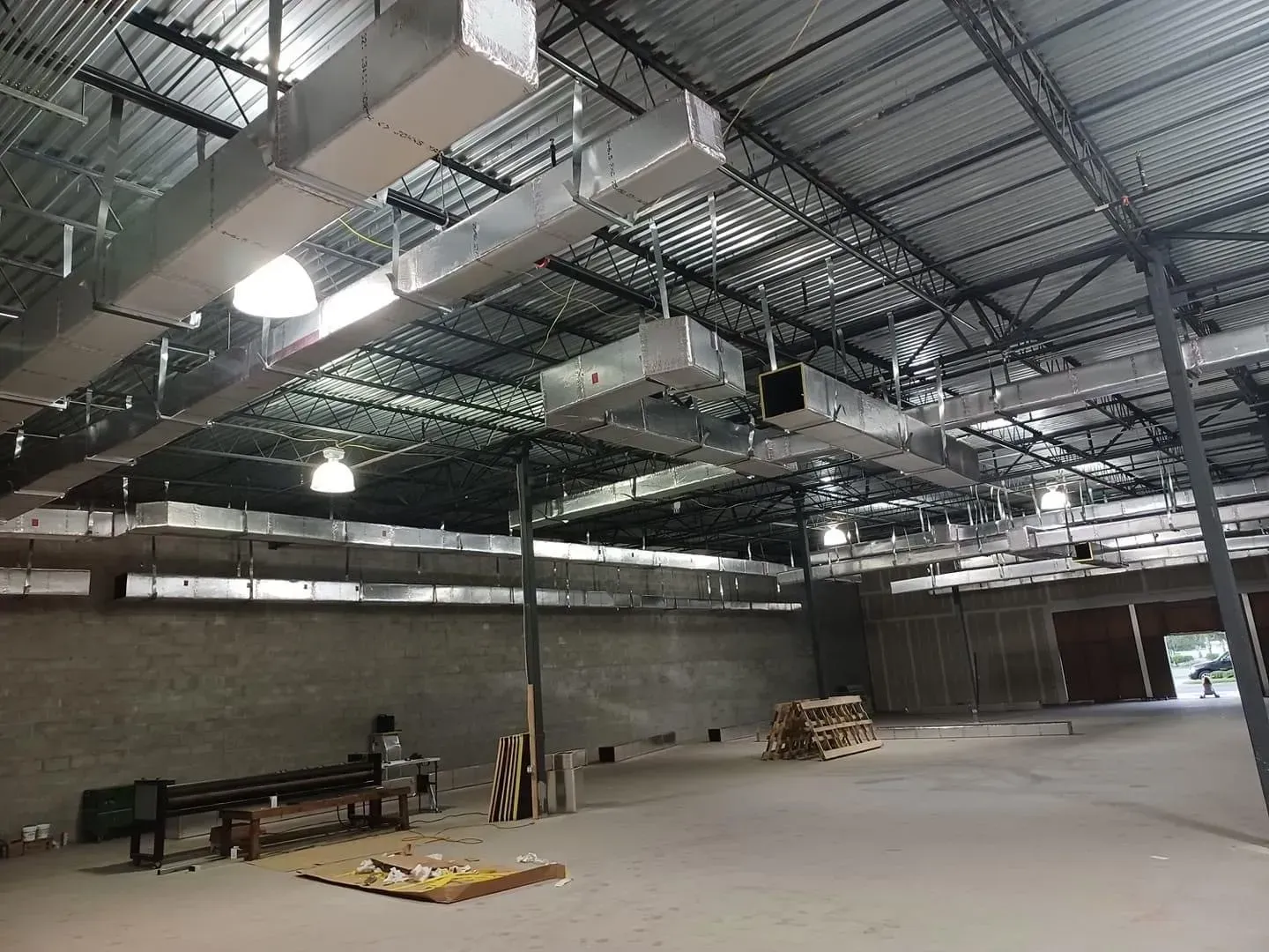 Interior of a building under construction, metal ductwork, concrete walls, and a person working on the floor.