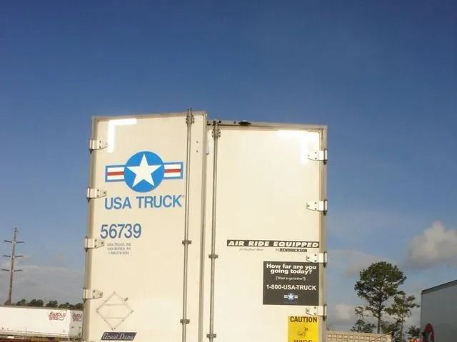 Rear doors of a white USA Truck trailer with a blue star logo against a blue sky.