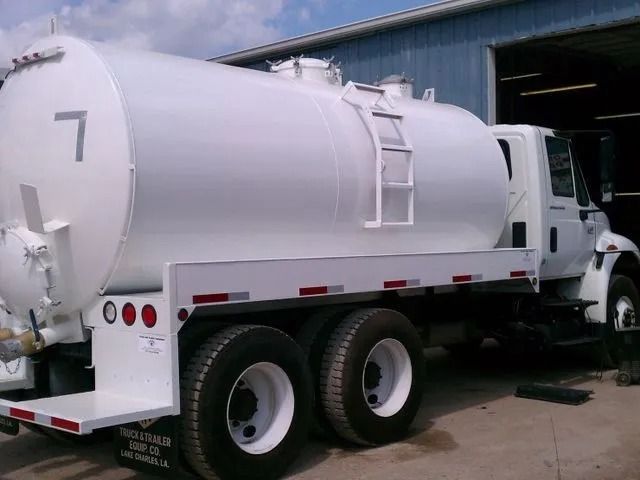 White tanker truck with a large tank and ladder parked outdoors.