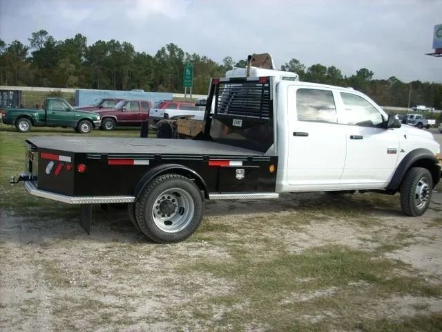 White flatbed truck with black bed and cab guard, parked on gravel with other vehicles in the background.