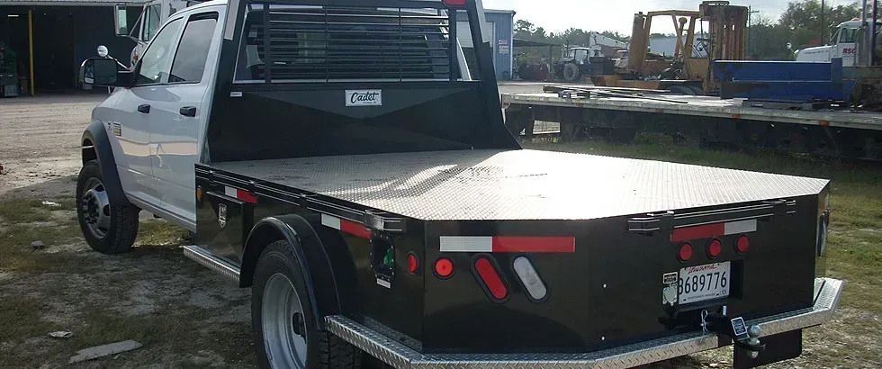 White flatbed truck with black bed, parked on a paved lot.